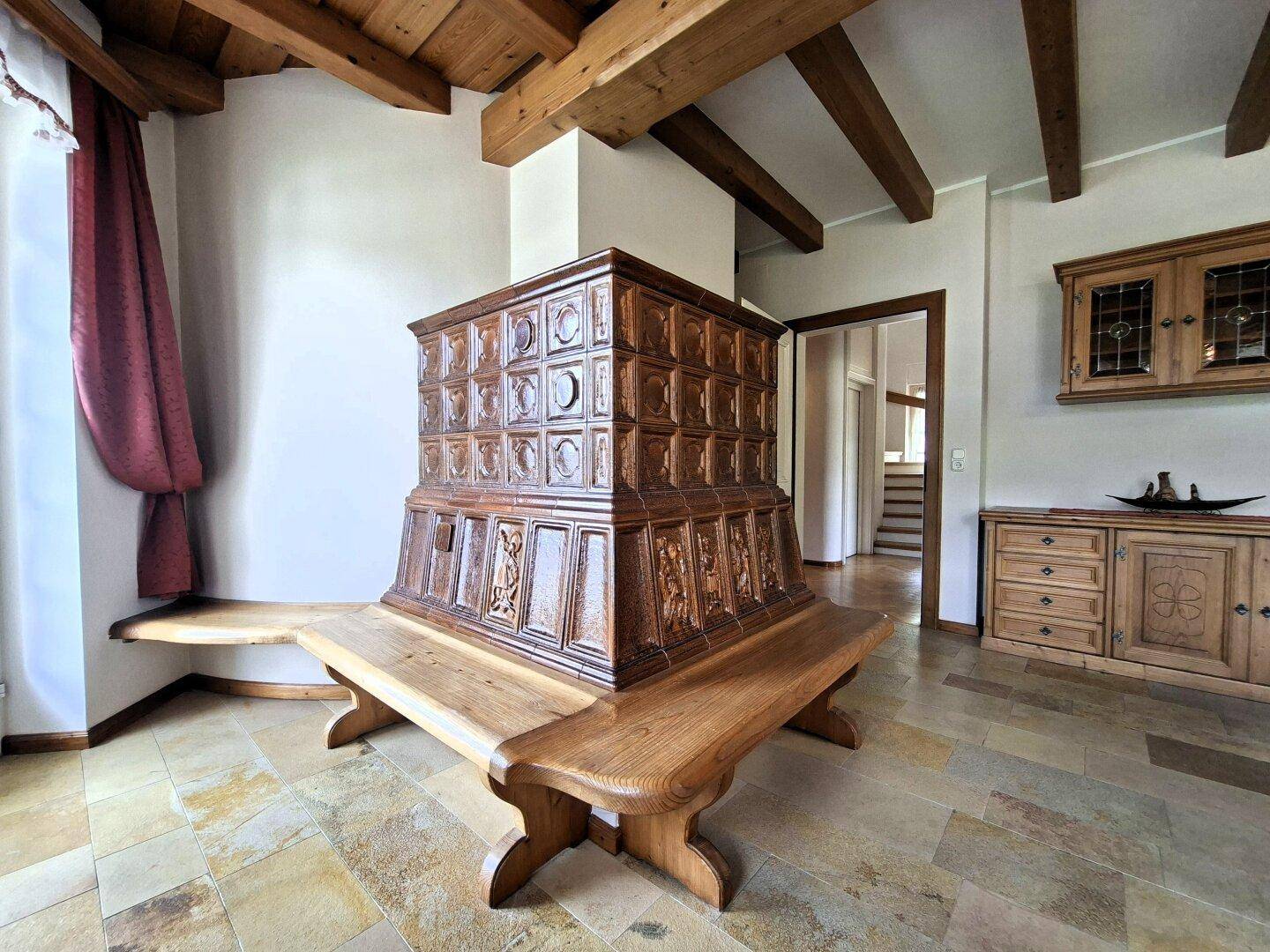 Gemütlicher Eingangsbereich mit traditionellem Kachelofen, Holzbalkendecke und Steinboden.