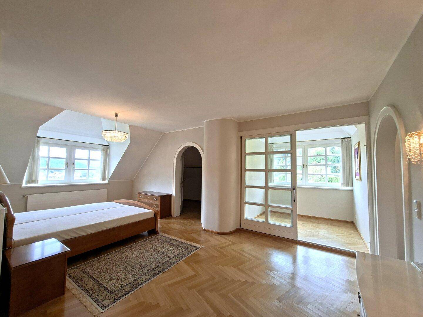 Helles Schlafzimmer mit Parkettboden, Dachschrägen und Schiebetür zu einem weiteren Raum.