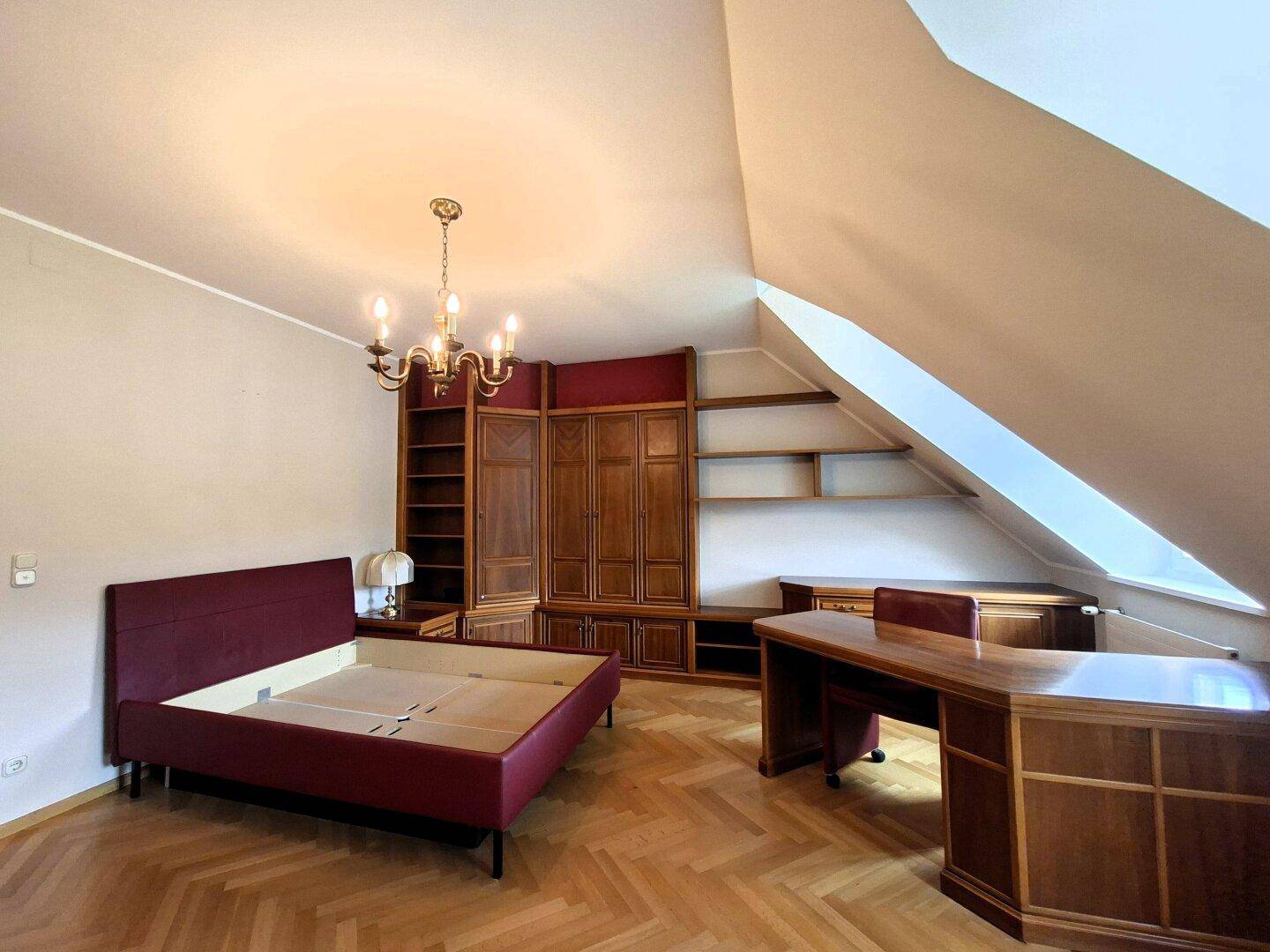 Geräumiges Schlafzimmer mit Parkettboden, Dachschrägen und integrierten Holzmöbeln.