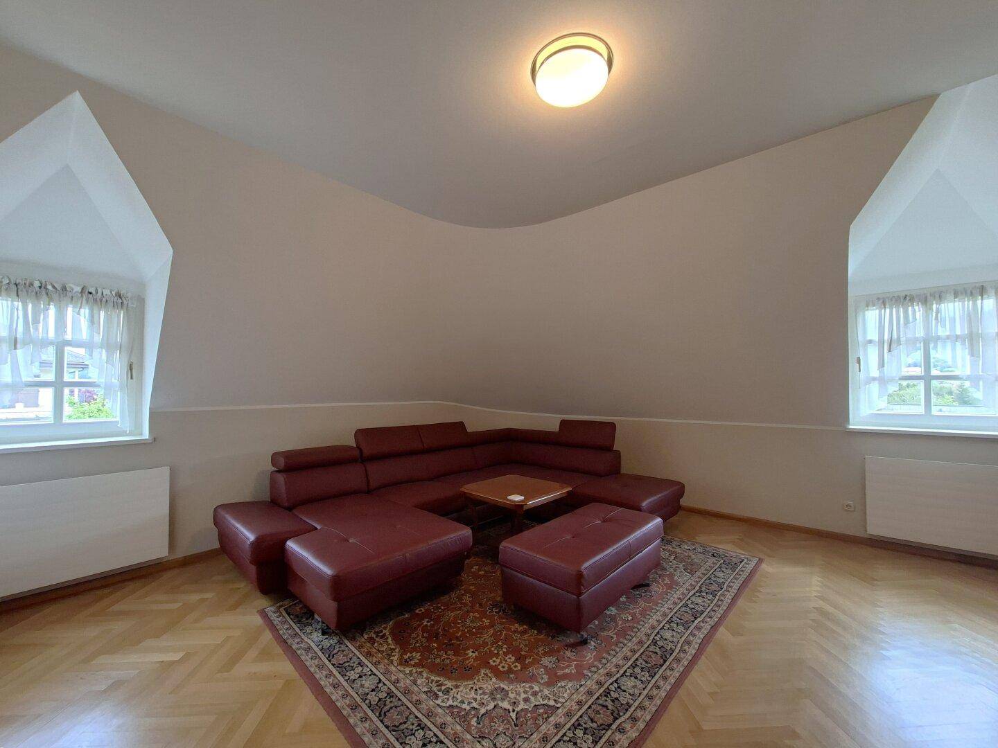 Gemütlicher Wohnbereich mit Ecksofa, Teppich und Fenstern in den Dachschrägen.