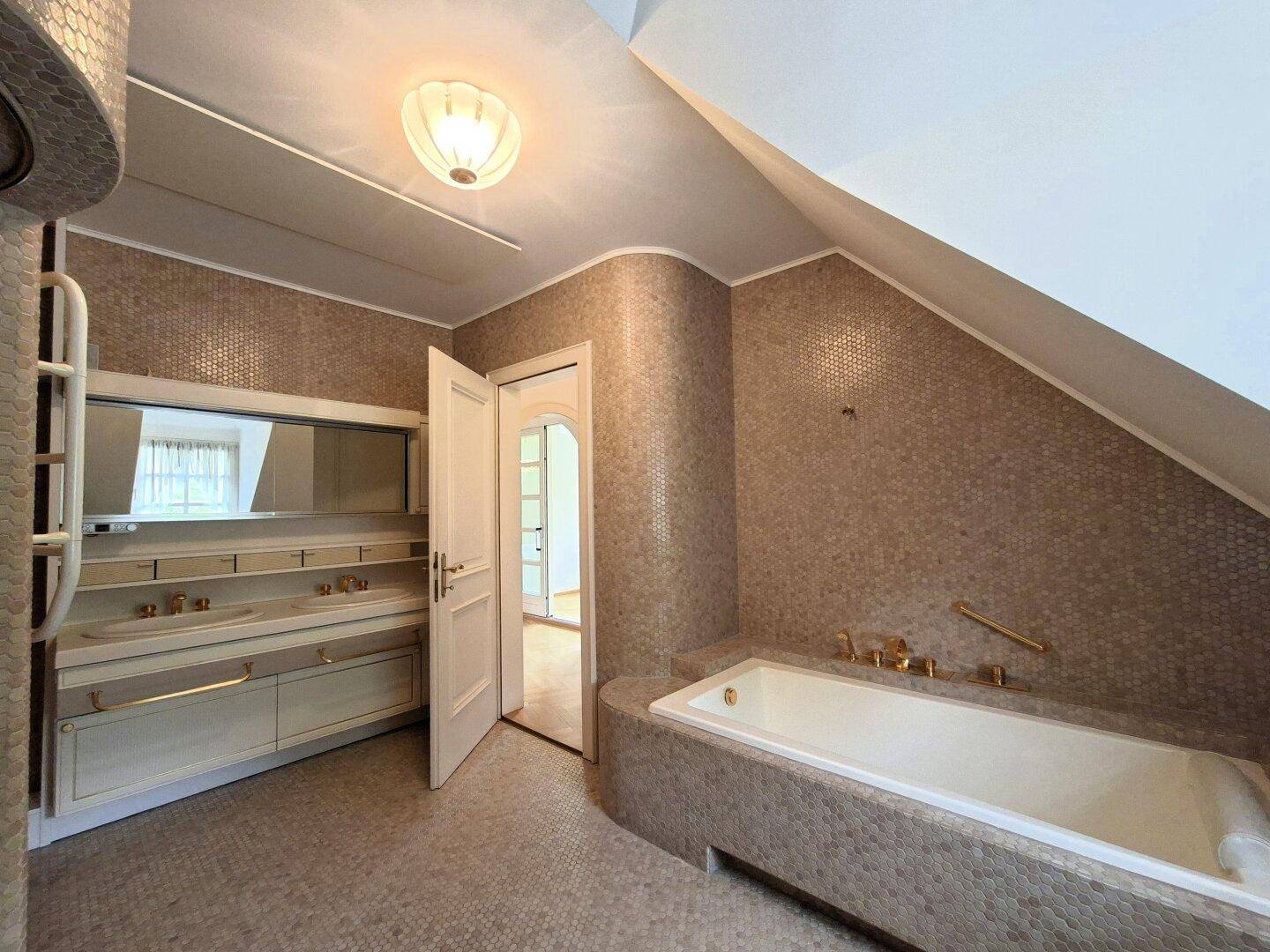Badezimmer mit Badewanne, Doppelwaschbecken und Mosaikfliesen in warmen Brauntönen.