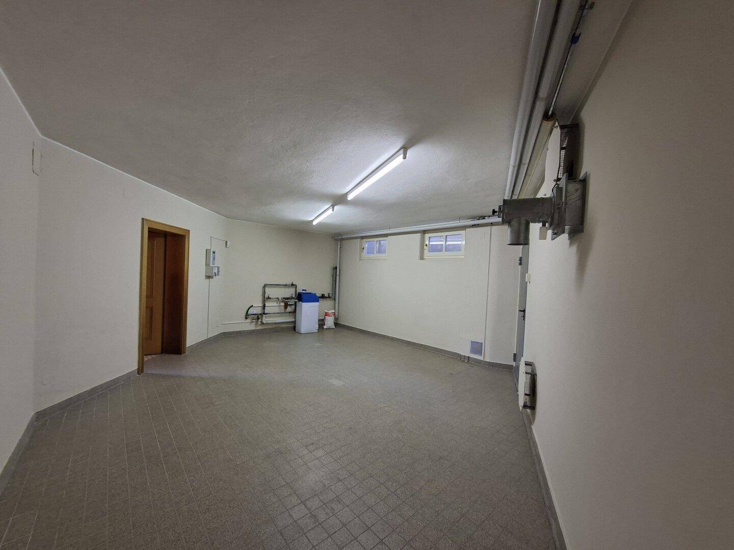 Geräumige Garage mit Fliesenboden und Fenstern, ideal für Fahrzeuge und Lagerung.