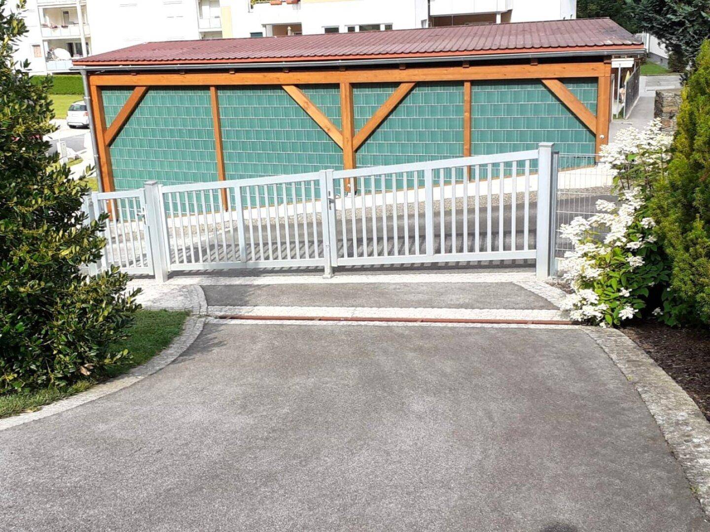 Moderner Carport mit Holzbalkenkonstruktion und sicherem Eingangstor zur Liegenschaft.