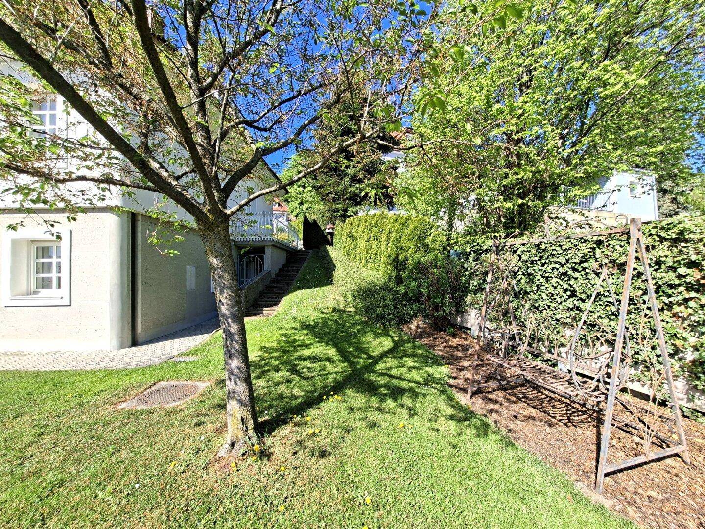 Gepflegter Gartenbereich mit Rasenfläche, Bäumen und einer Schaukel im Grünen.