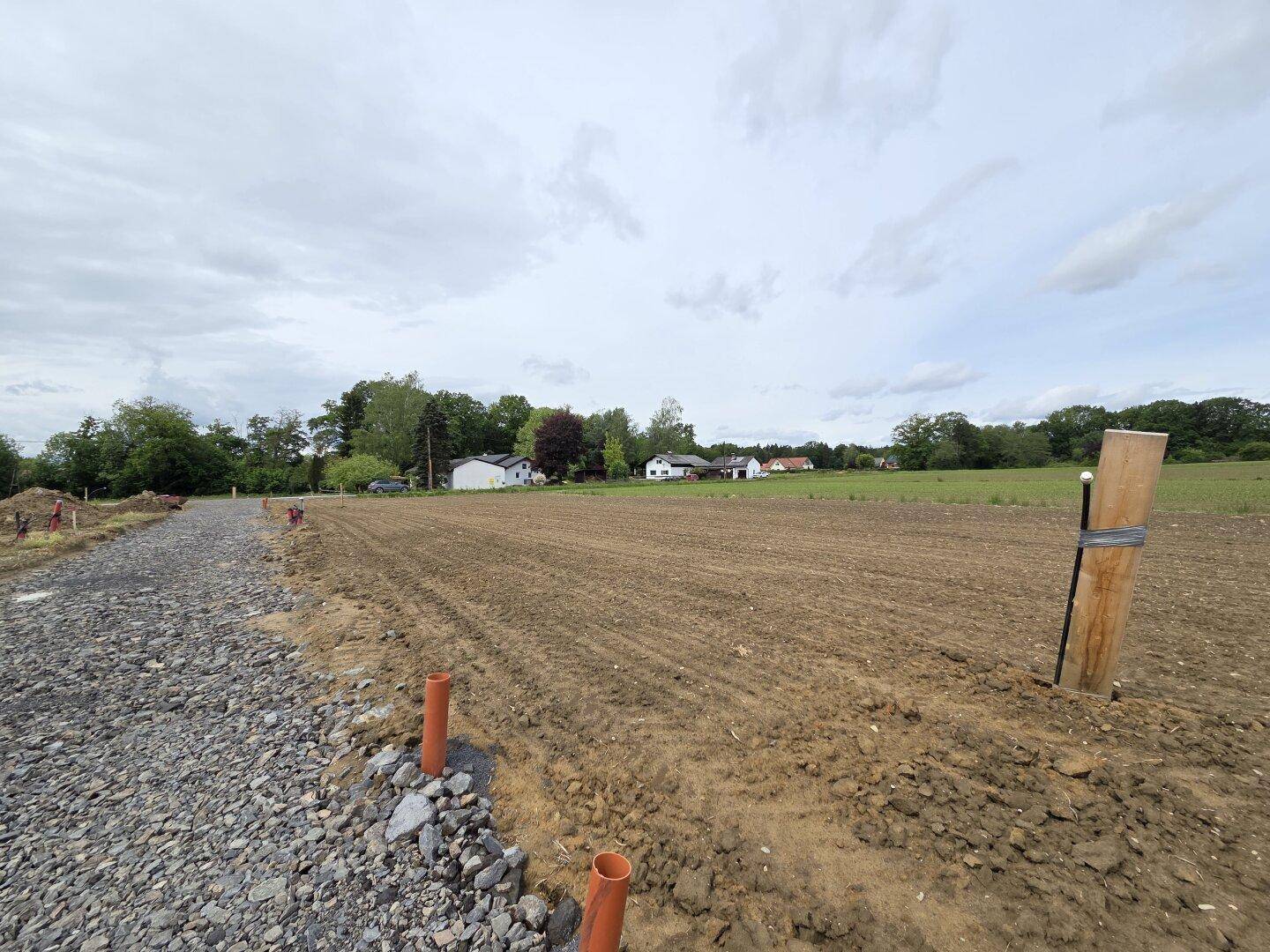Blick über das vorbereitete Baugrundstück mit Schotterweg und ländlicher Umgebung.