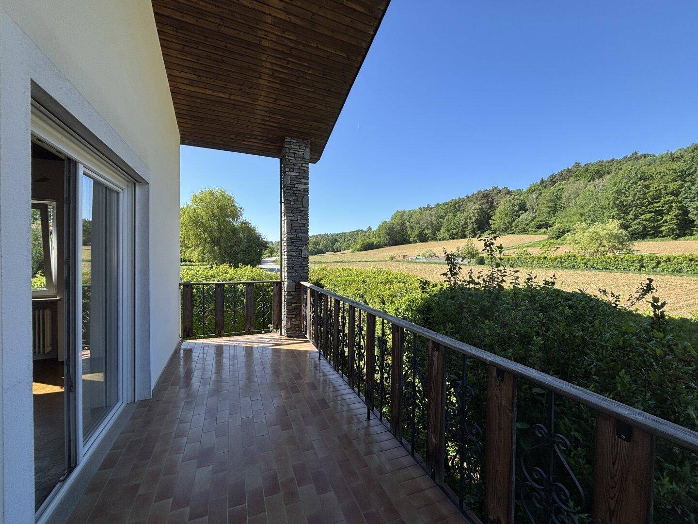 Überdachter Balkon mit Fliesenboden und schmiedeeisernem Geländer, bietet weiten Blick auf Weinberge.