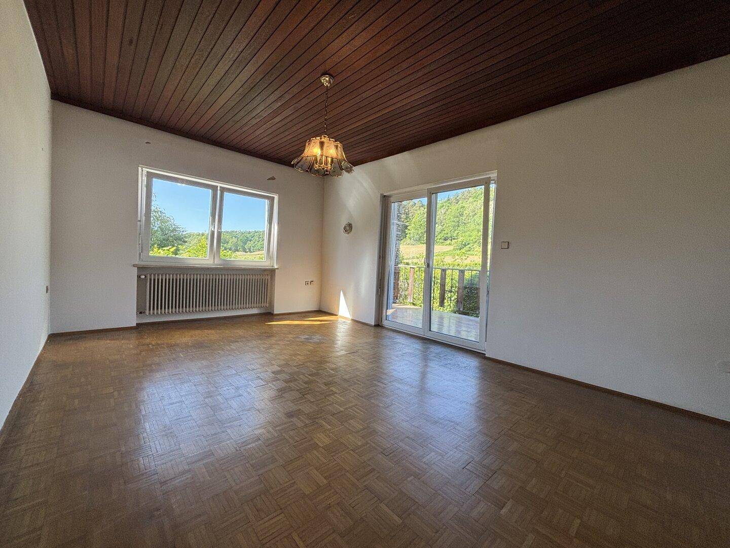 Helles Wohnzimmer mit Parkettboden, Holzdach und Zugang zu einem Balkon mit Weitblick.