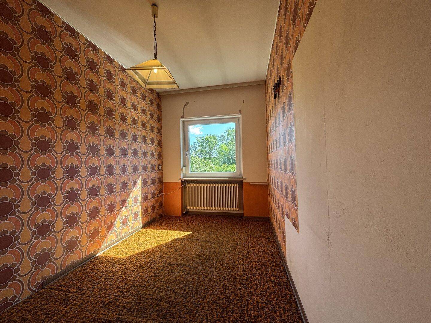 Schlafzimmer mit auffälliger gemusterter Tapete und Teppichboden, bietet Blick ins Grüne.