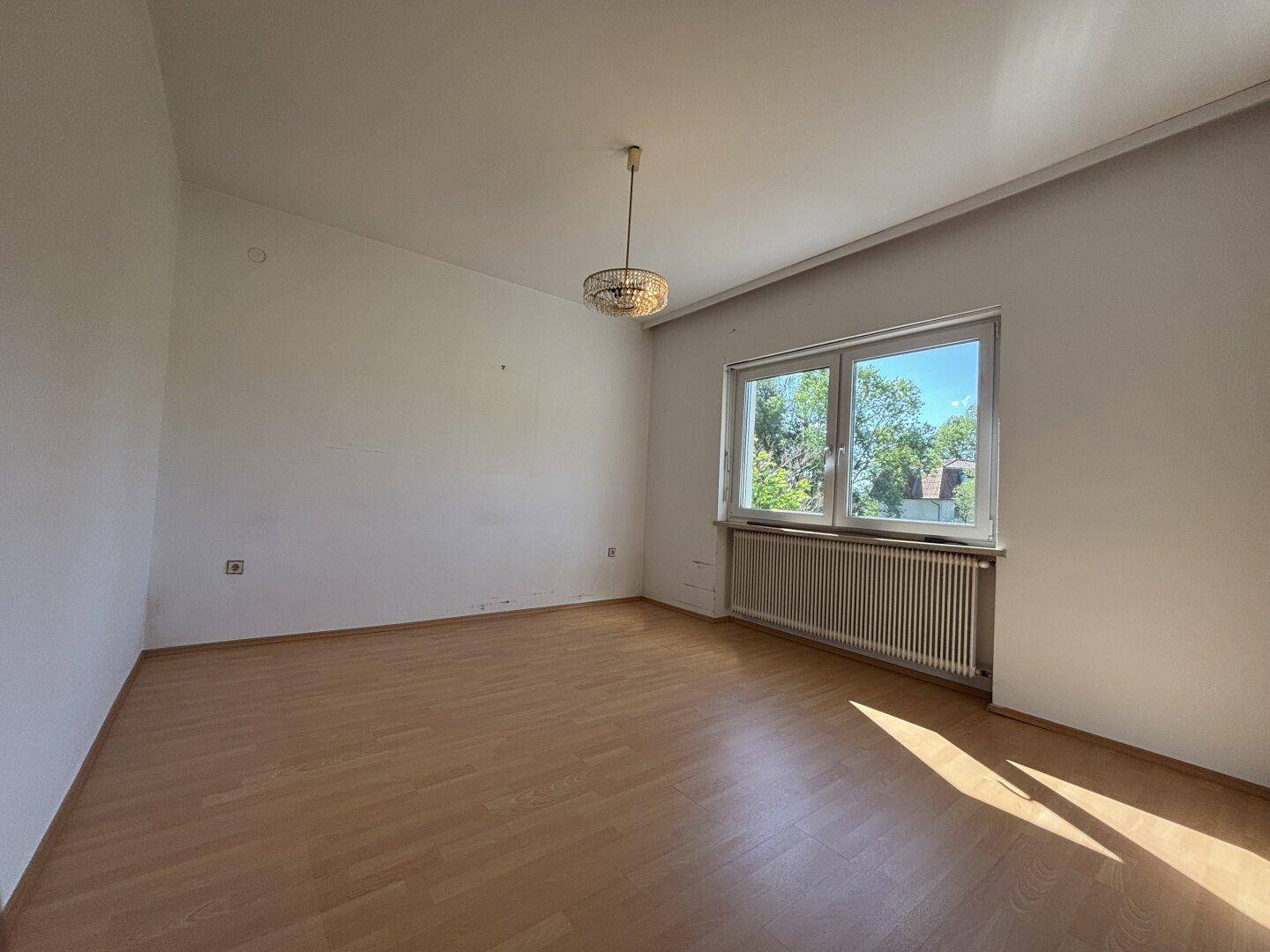 Geräumiges Schlafzimmer mit hellem Holzboden und großem Fenster, das eine grüne Aussicht bietet.