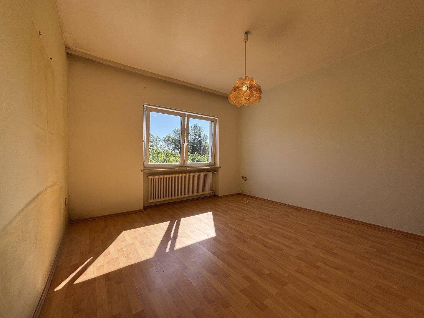 Helles Schlafzimmer mit Holzboden und großem Fenster, das viel Tageslicht hereinlässt.