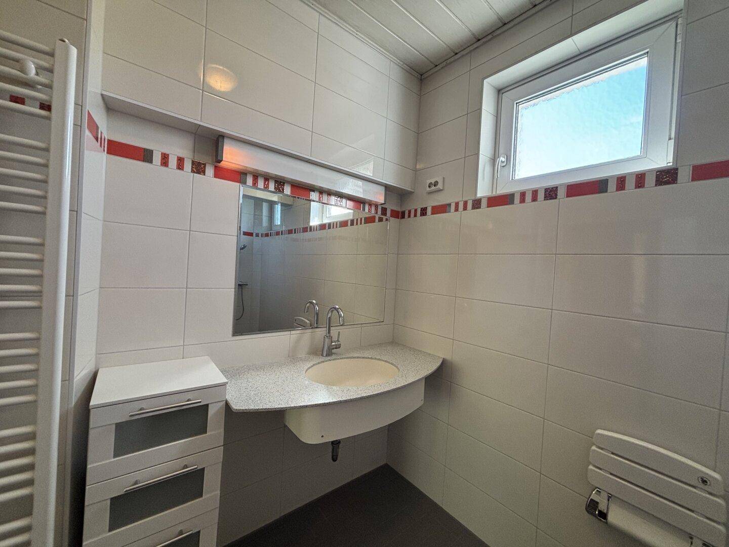 Modernisiertes Badezimmer mit weißen Fliesen, Einzelwaschbecken und beheiztem Handtuchhalter.