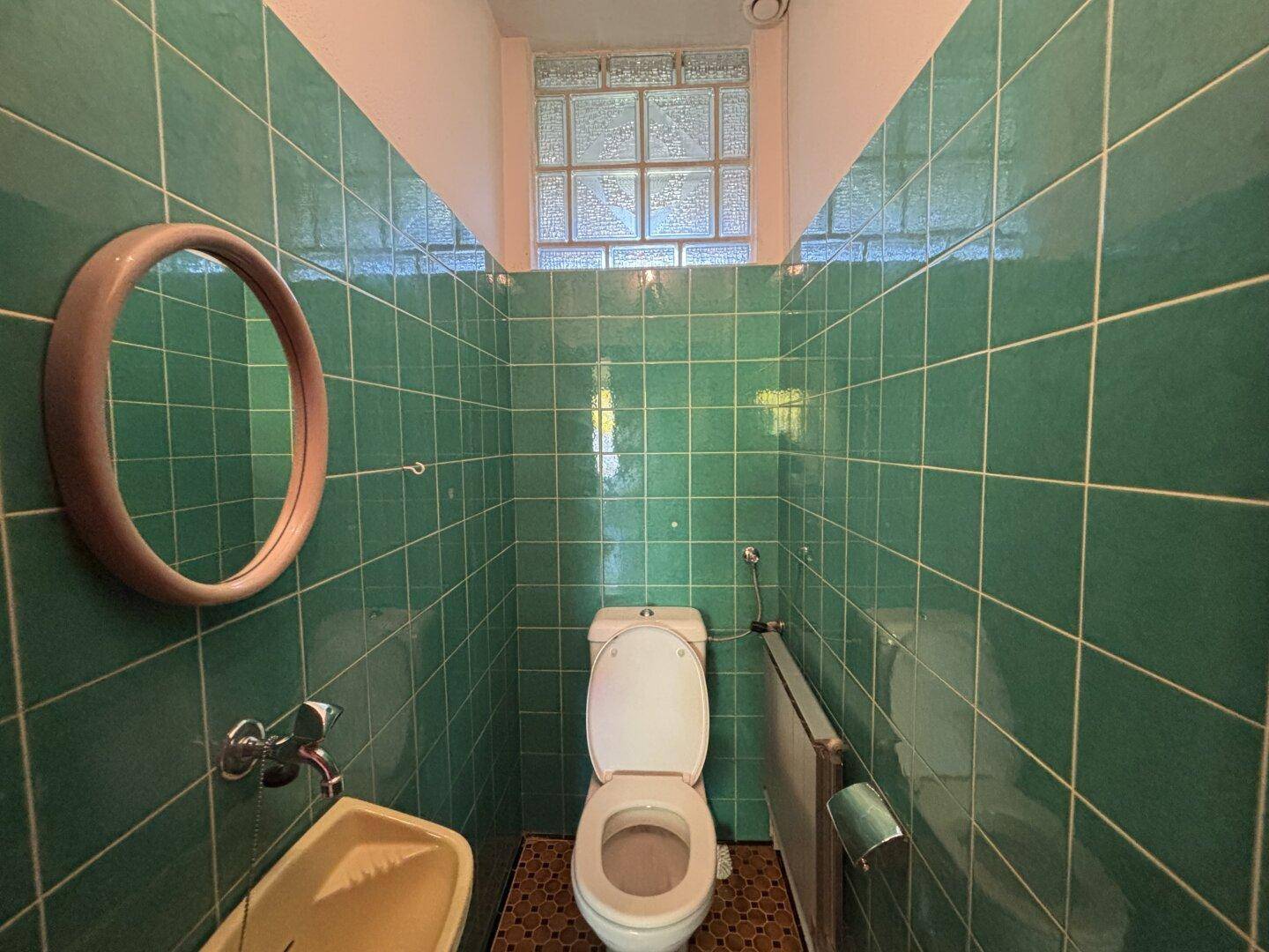 Kleines WC mit grünen Fliesen, Toilette und einem kleinen Waschbecken.