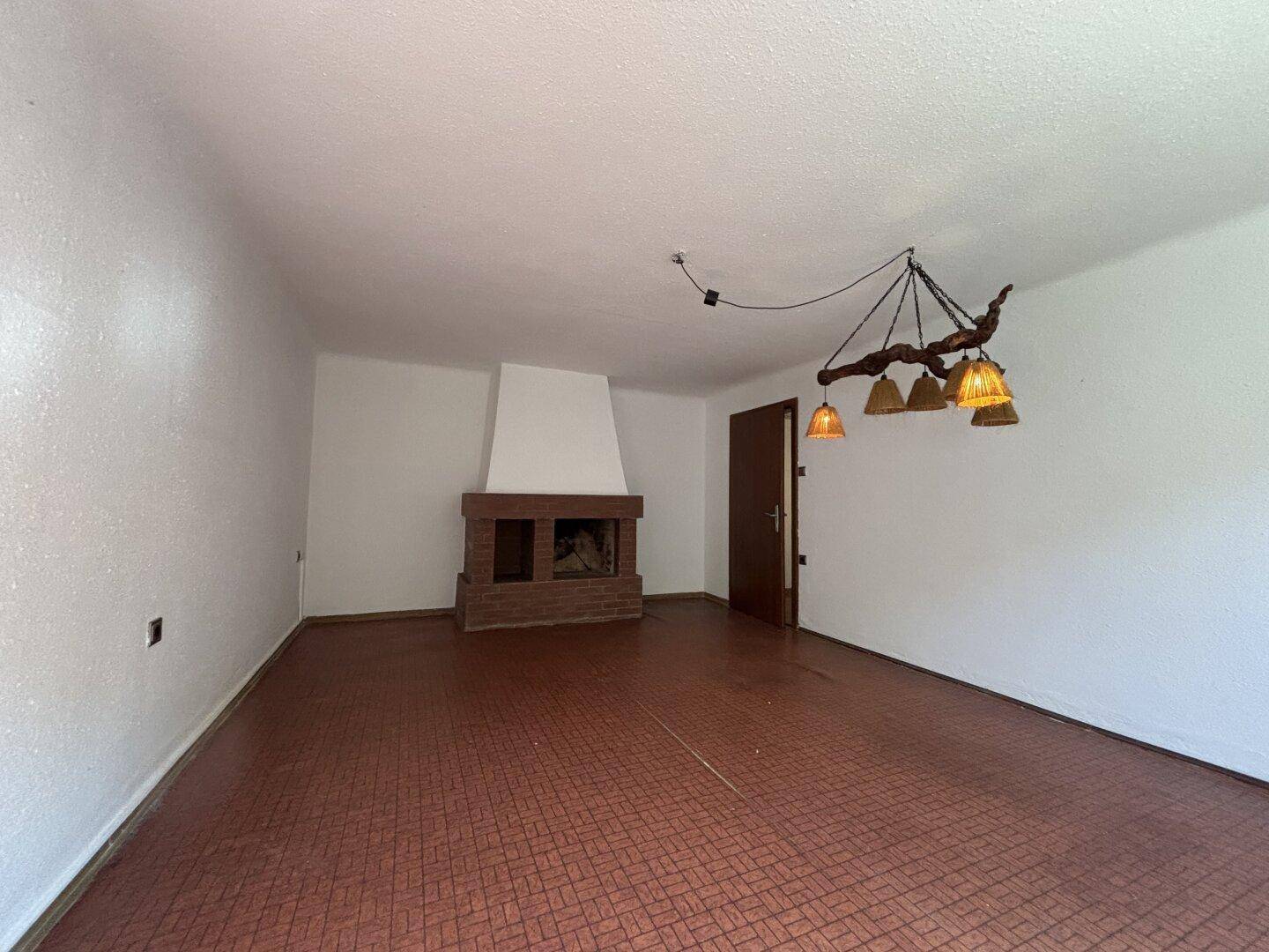 Wohnzimmer mit Kamin, dunklem Boden und rustikaler Deckenleuchte, bereit zur Gestaltung.