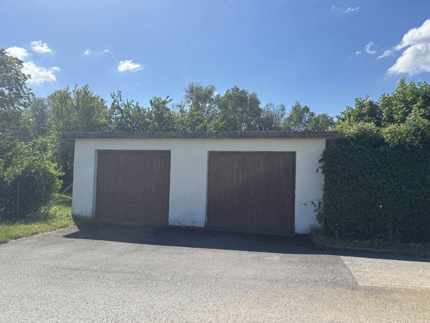 Freistehende Doppelgarage mit zwei Holztoren, umgeben von grünen Hecken.