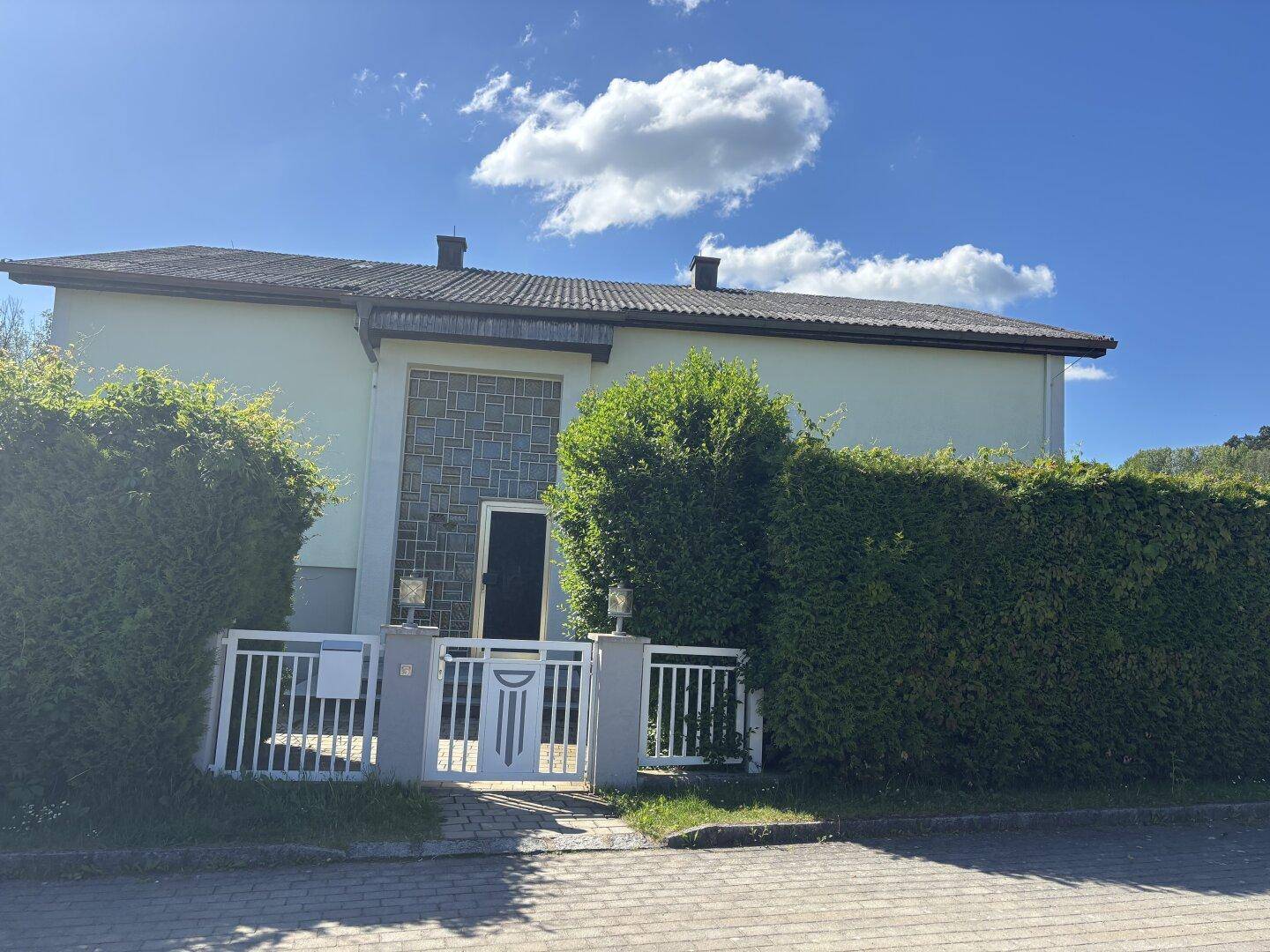 Vorderansicht des Hauses mit Eingangsbereich, Zaun und gepflegten Hecken.