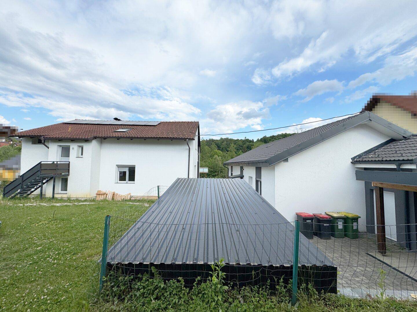 Rückansicht des Hauses mit Garten und Blick auf die umliegende Landschaft unter blauem Himmel.