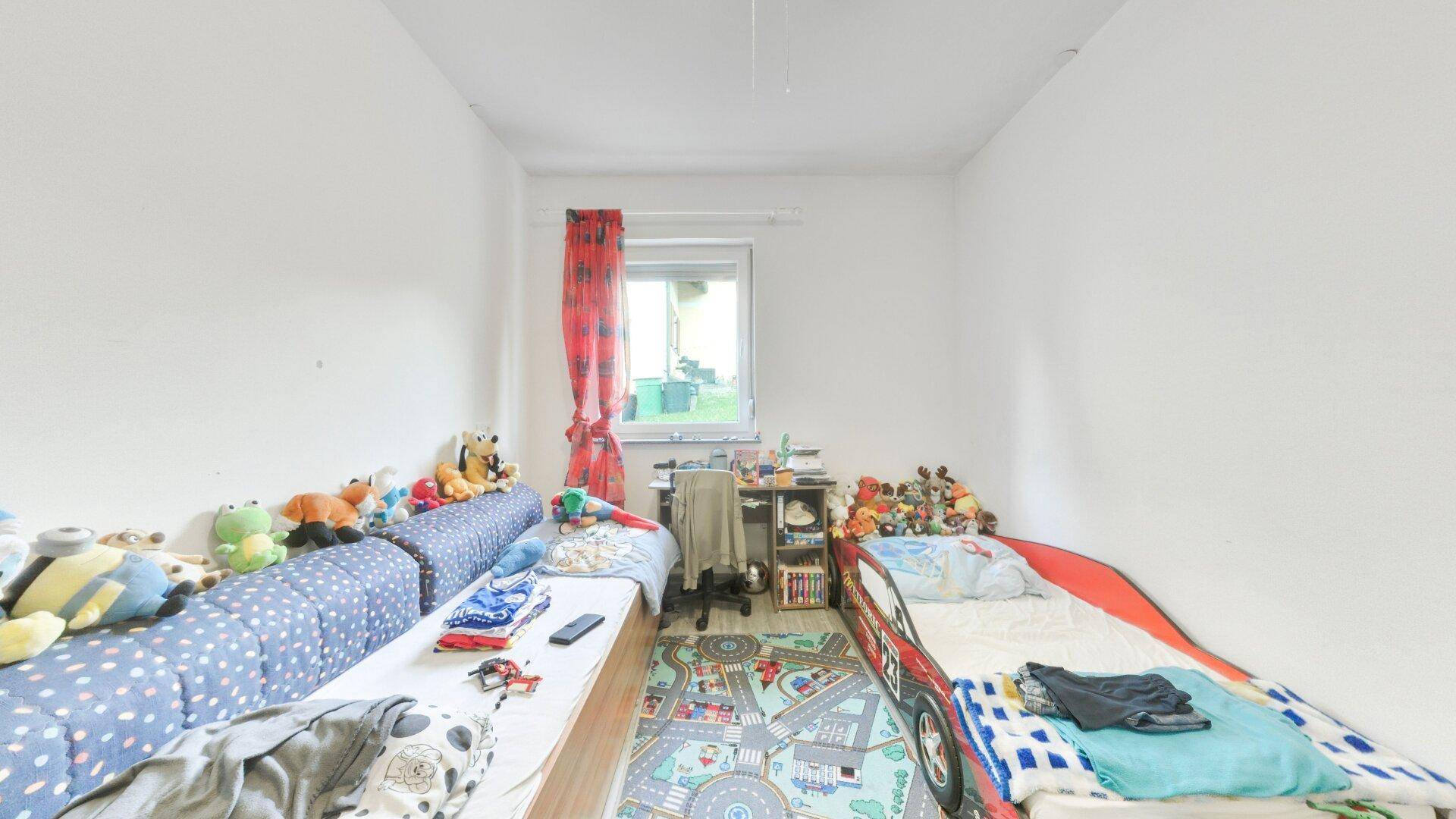 Kinderzimmer mit zwei Betten, Spielzeug und einem bunten Teppich, hell und freundlich gestaltet.