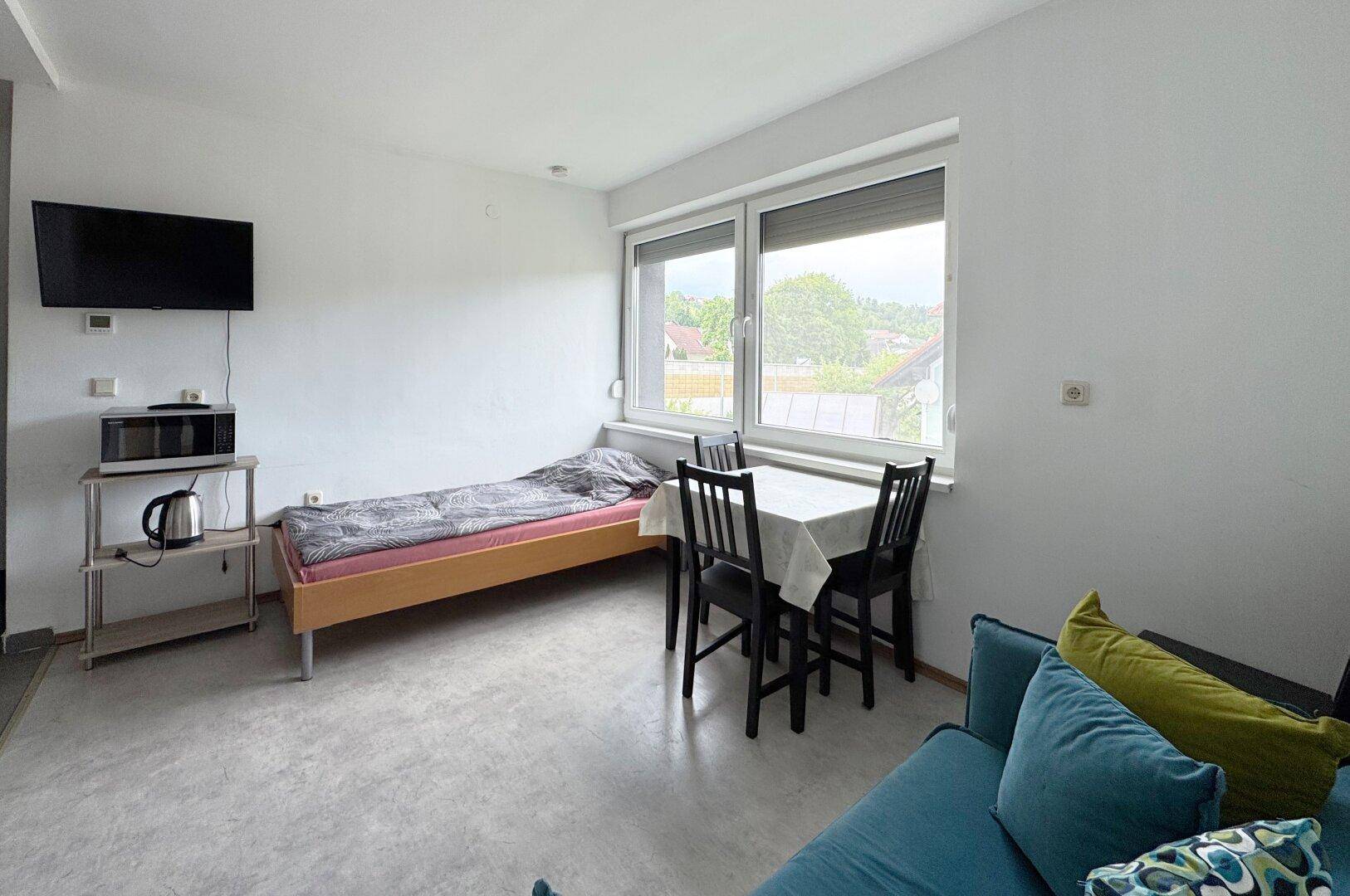 Heller Wohnbereich mit Einzelbett, Esstisch und Sofa, ideal für Gäste oder als Studio.