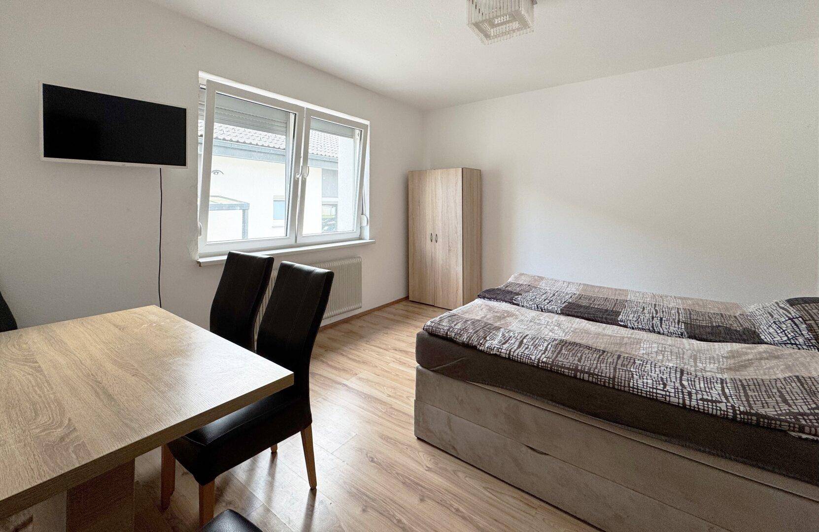 Schlafzimmer mit Doppelbett, Esstisch und Fernseher, hell und funktional eingerichtet.