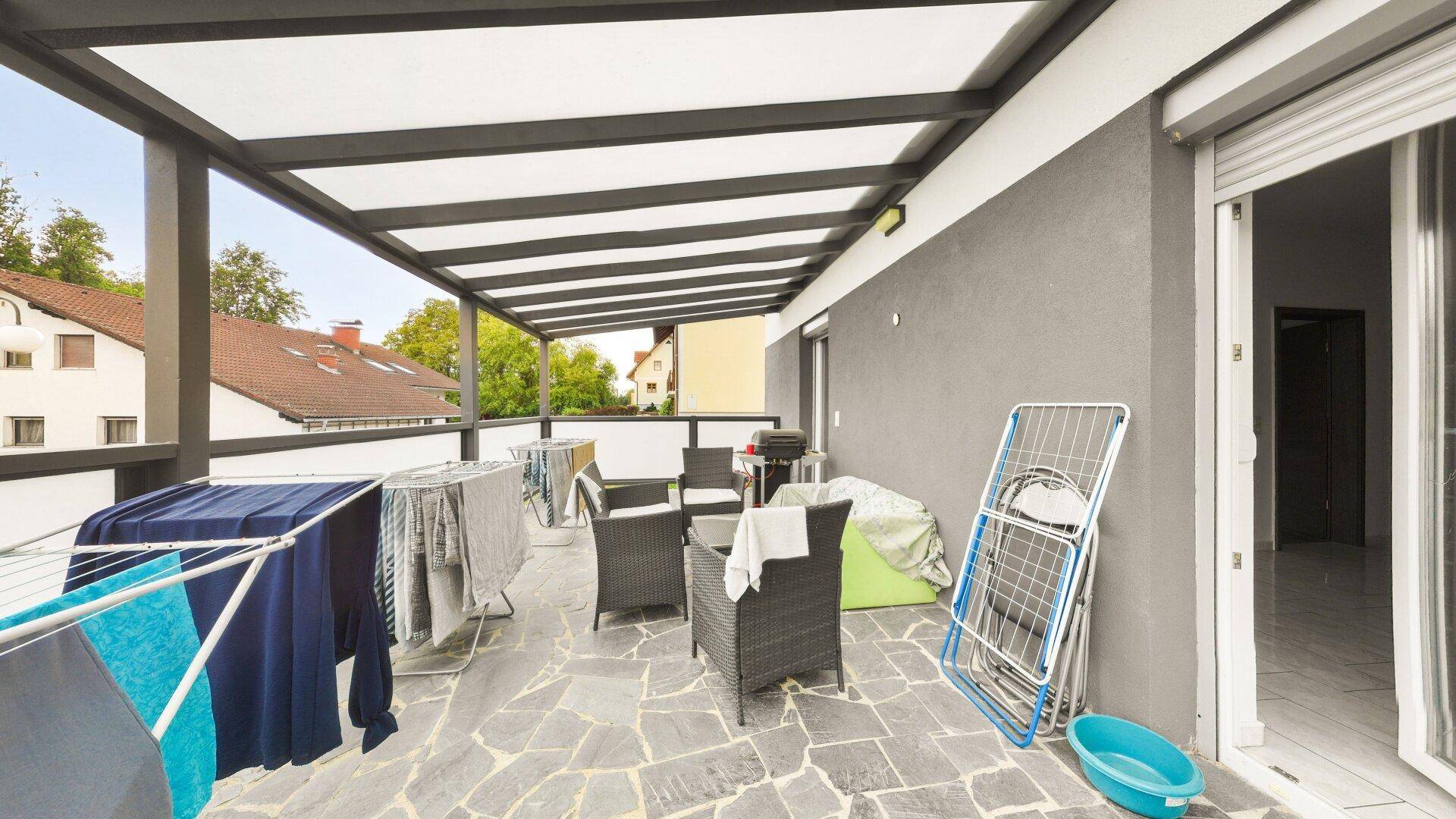 Überdachte Terrasse mit Steinboden und Gartenmöbeln, ideal zum Entspannen im Freien.