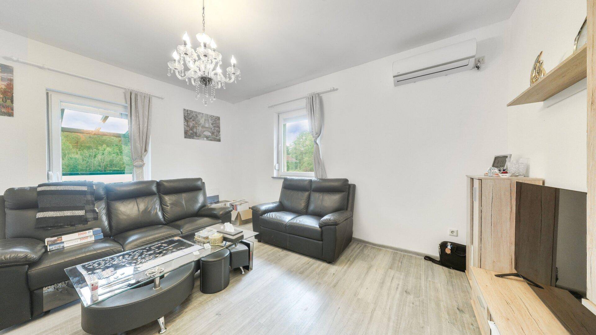 Geräumiges Wohnzimmer mit Ledersofas, Kronleuchter und Klimaanlage, hell und modern.