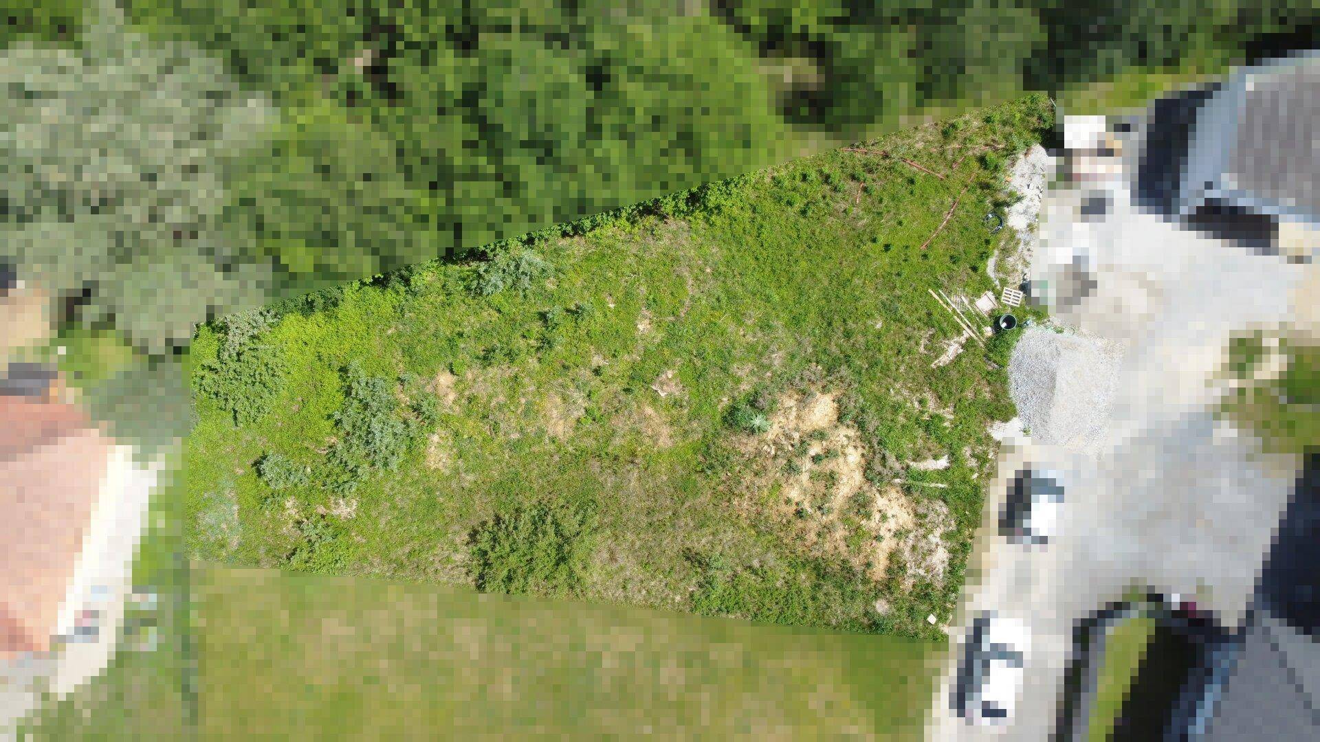 Luftaufnahme eines unbebauten Grundstücks, umgeben von Wald und Wohnbebauung.