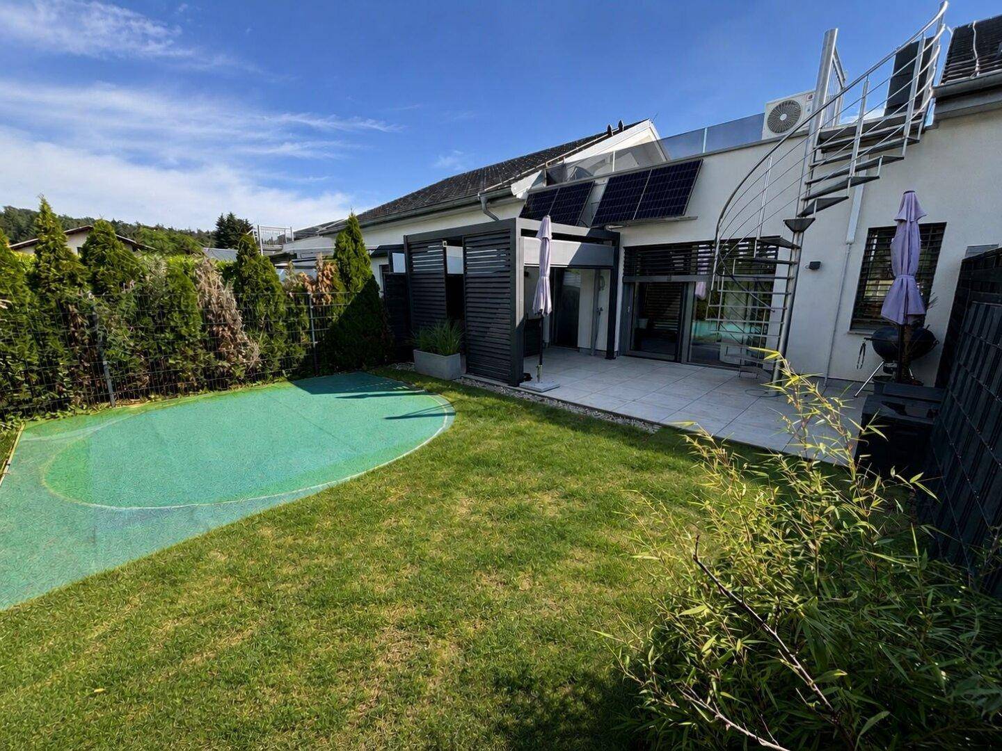 Gepflegter Garten mit Rasenfläche, Terrasse und Photovoltaikanlage am modernen Haus.