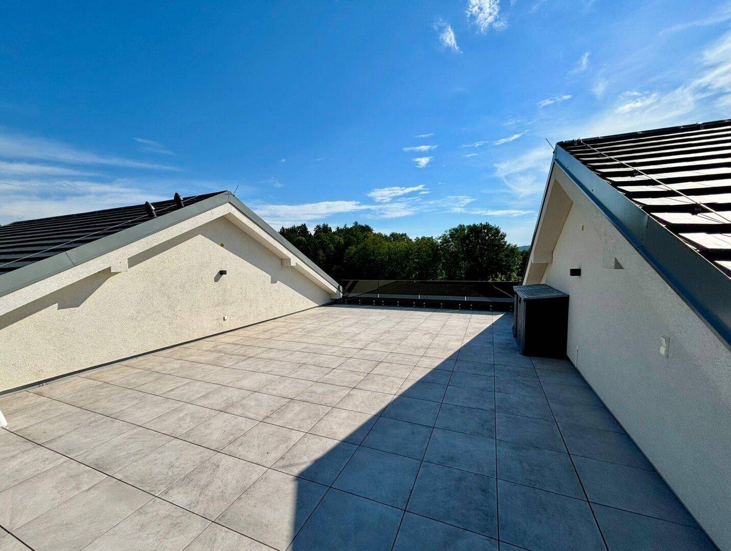 Großzügige Dachterrasse mit modernen Fliesen, weitem Blick und viel Sonnenlicht.