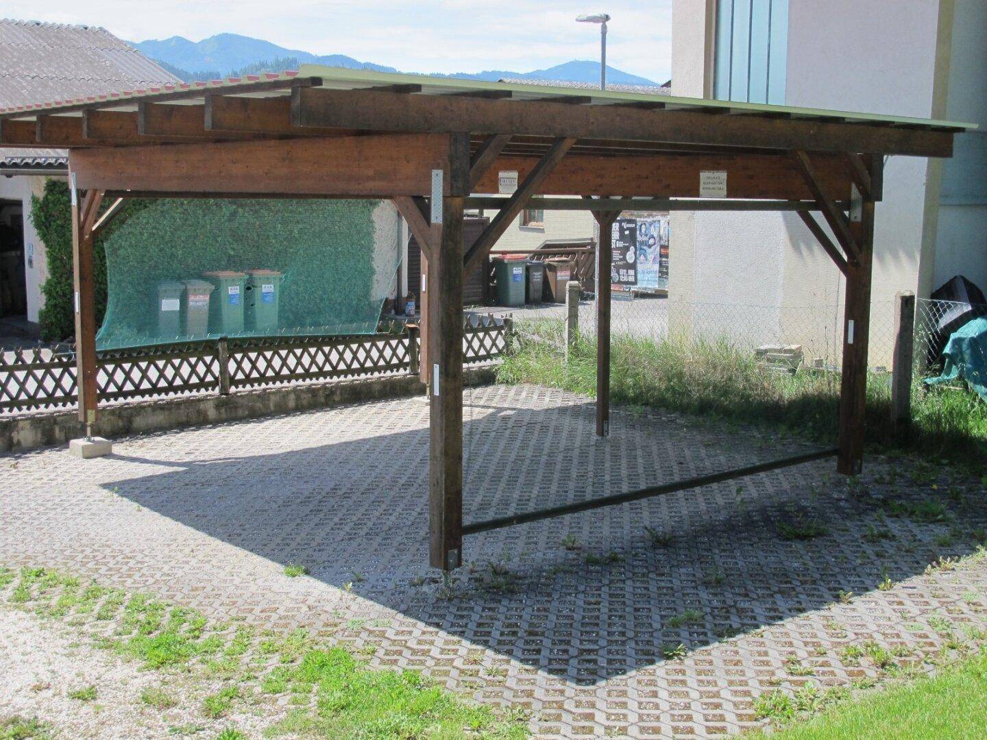 Robuster Holzcarport auf gepflastertem Untergrund, bietet geschützten Stellplatz für Fahrzeuge.