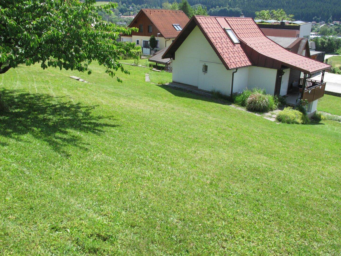 Gepflegte Rasenfläche vor einem Wohnhaus mit rotem Dach und kleinem Balkon.