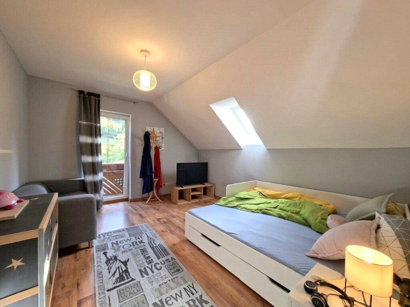 Helles Schlafzimmer mit Holzboden, Dachschräge und Zugang zu einem kleinen Balkon.