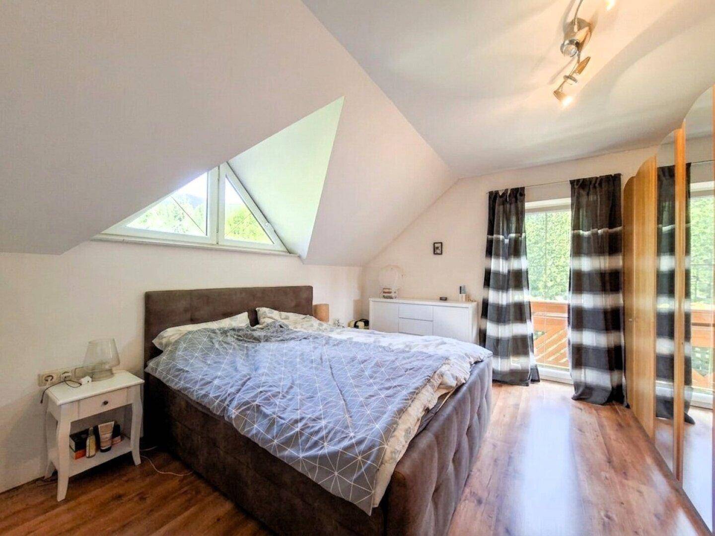 Geräumiges Schlafzimmer mit Holzboden, Dachschräge und großem Fenster mit Blick ins Grüne.