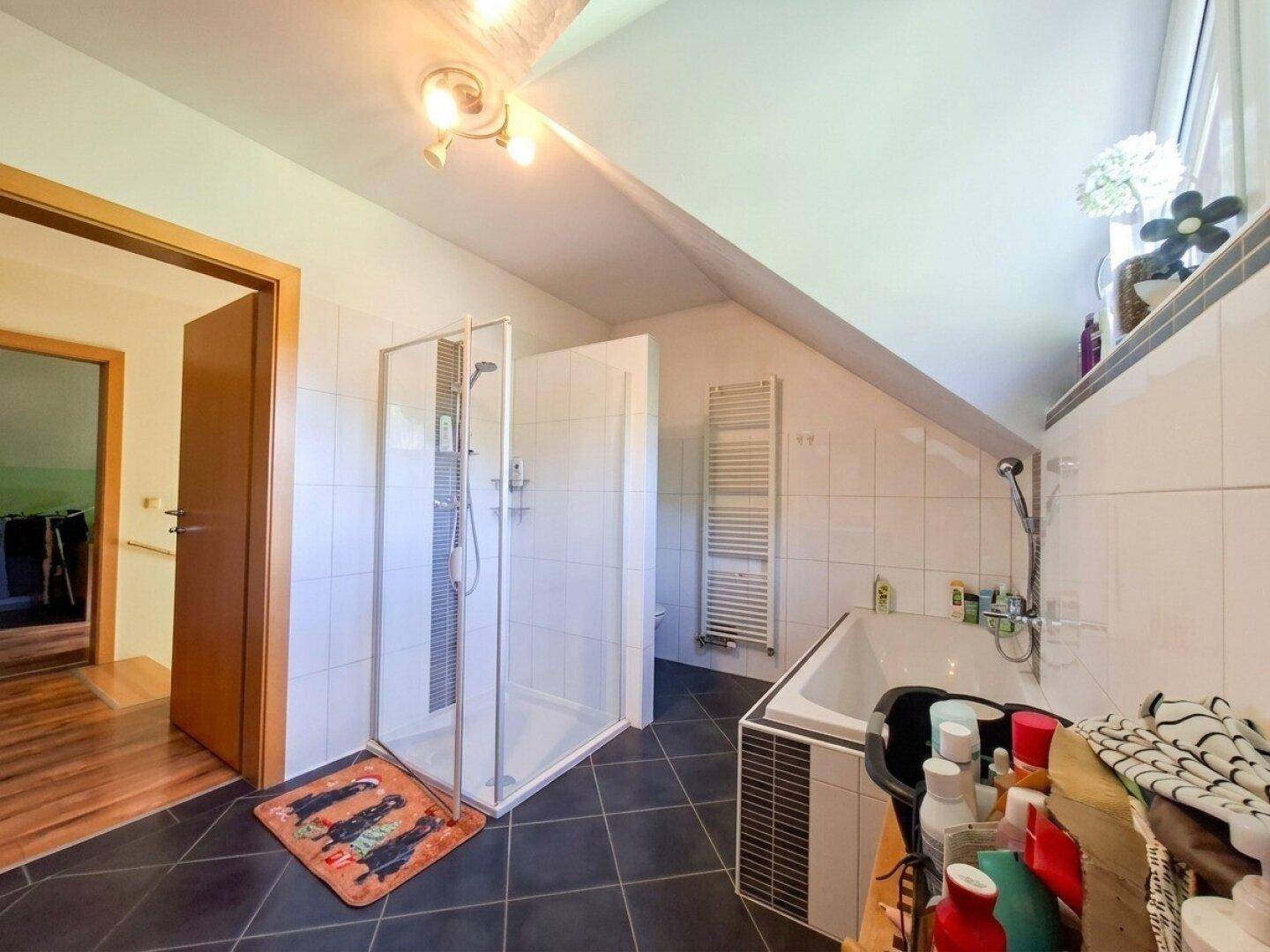 Modernes Badezimmer mit dunklen Fliesen, Dusche, Badewanne und Dachschräge.