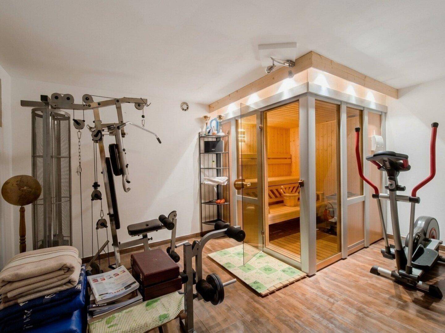 Fitnessraum mit verschiedenen Trainingsgeräten und einer integrierten Sauna für Wellness.