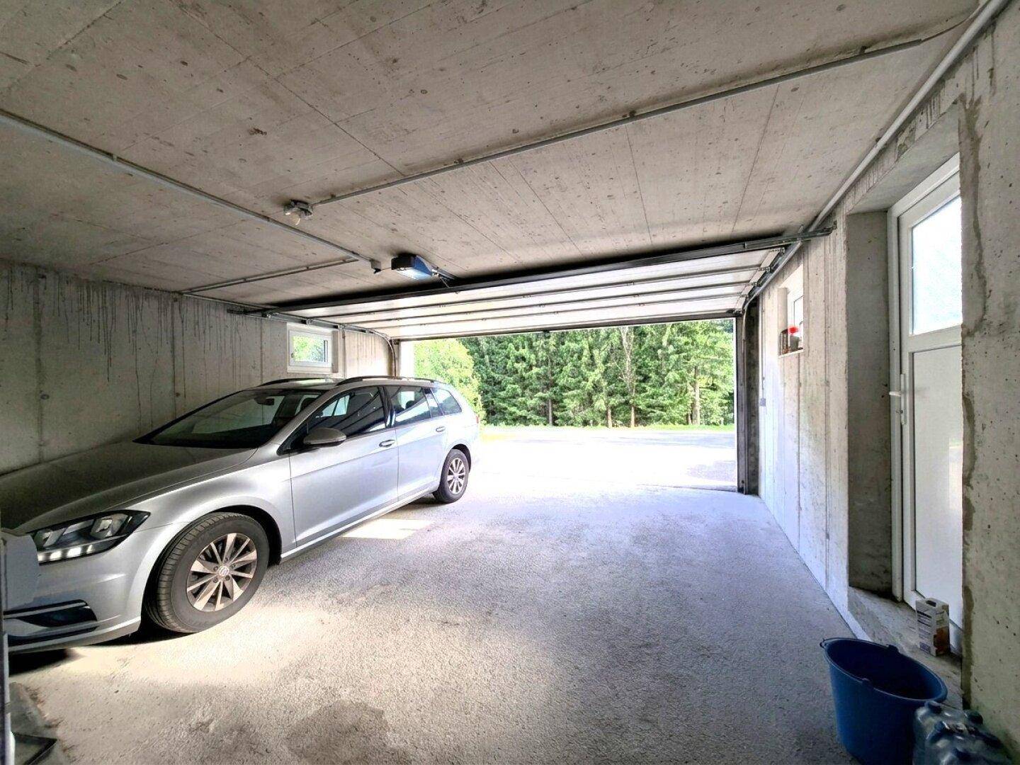 Geräumige Garage mit Betonboden und Platz für ein Fahrzeug, mit Blick ins Grüne.