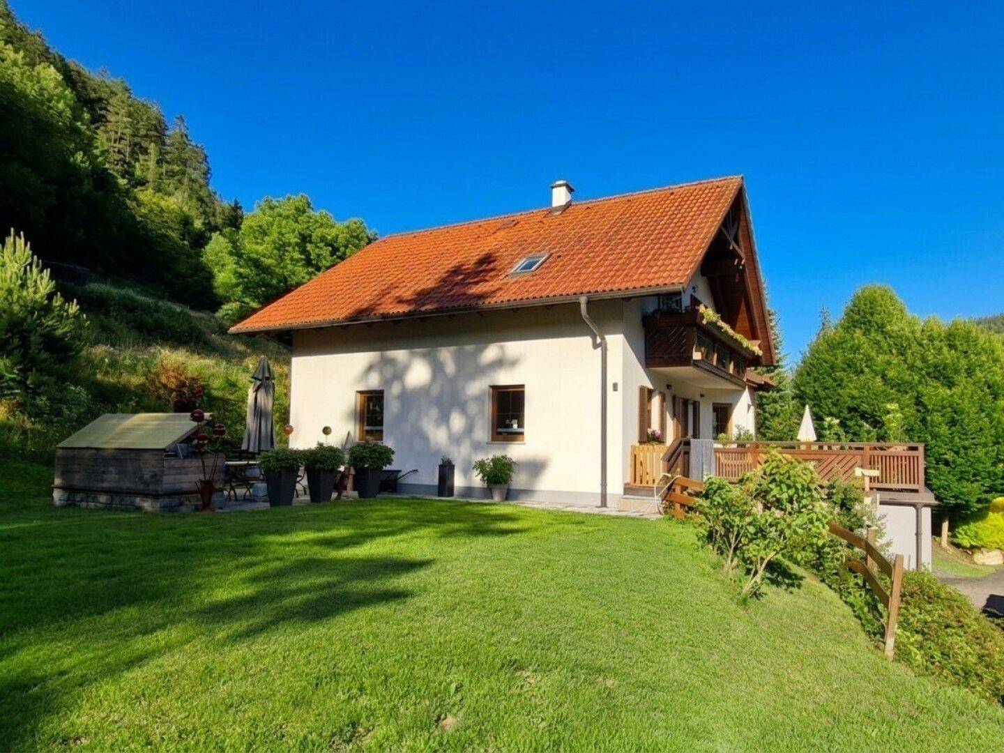 Rückansicht des Hauses mit gepflegtem Rasen, Terrasse und Blick auf die bewaldeten Hügel.