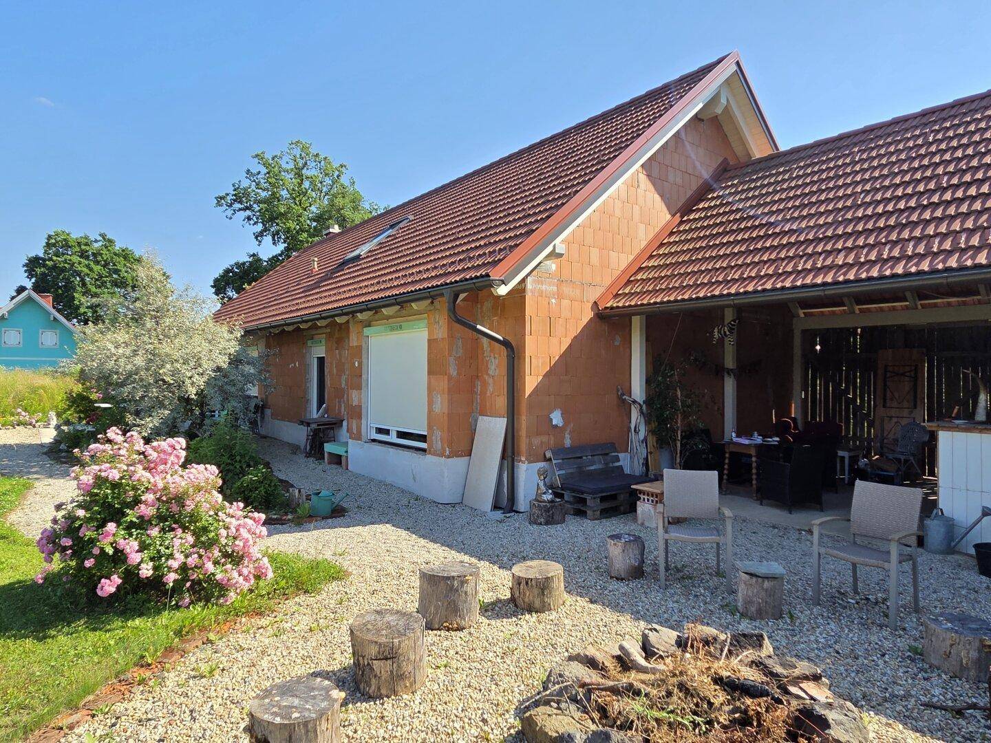 Gartenbereich mit Feuerstelle, Sitzgelegenheiten und blühenden Sträuchern.