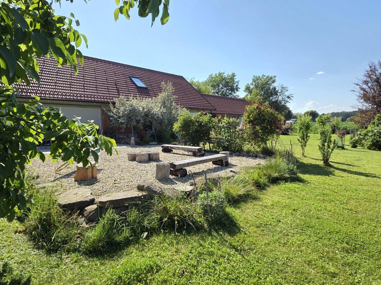 Entspannungsbereich im Garten mit Holzbänken und Blick auf die grüne Landschaft.