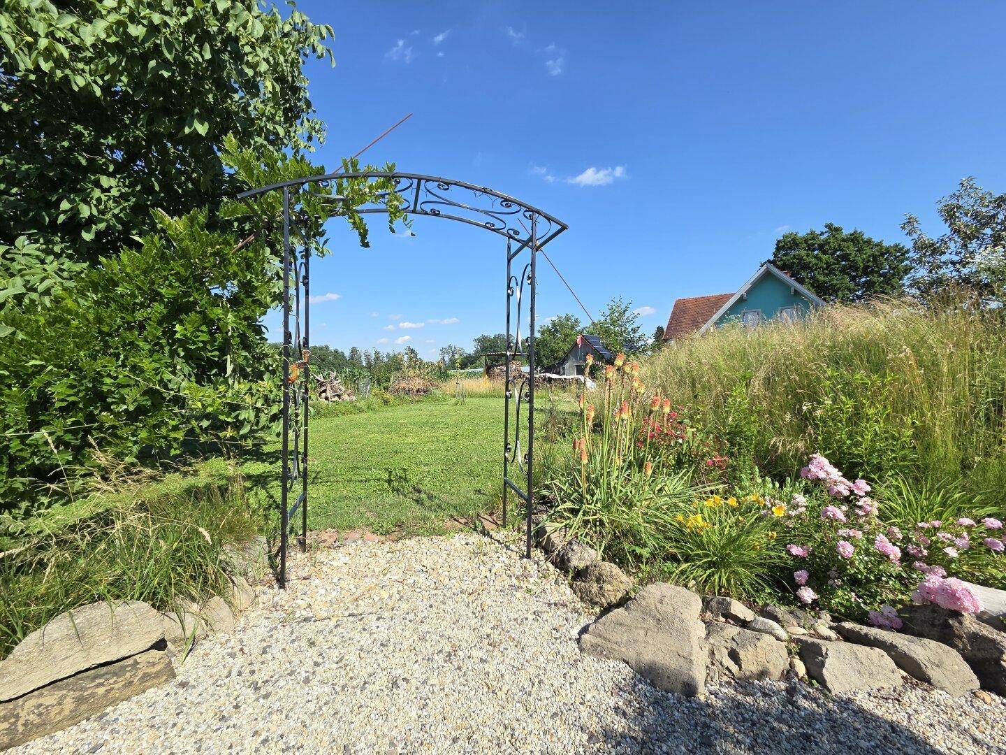Romantischer Gartenbogen führt zu einer weitläufigen Rasenfläche mit Blumenbeeten.