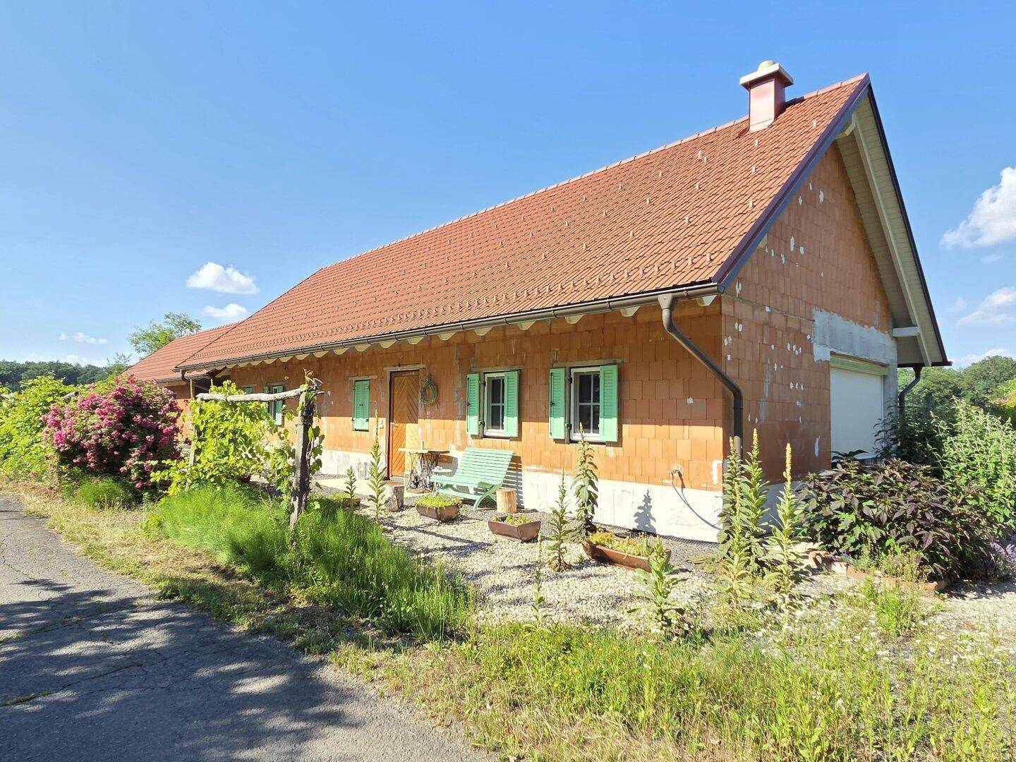 Ländliches Haus mit Holzfassade, grünen Fensterläden und Gartenbereich.