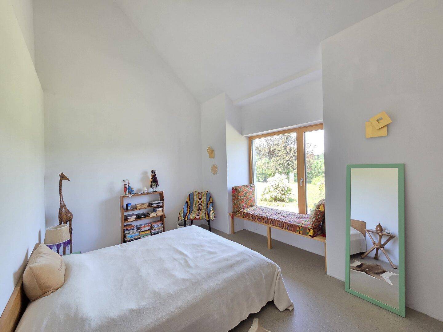 Geräumiges Schlafzimmer mit hohen Decken, Fensterbank und Blick in den Garten.