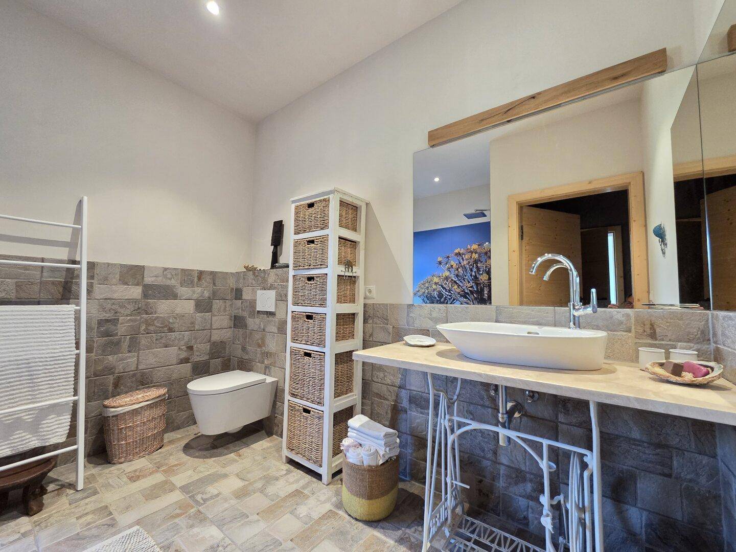 Modernes Badezimmer mit Waschtisch, Wand-WC und Steinoptik-Fliesen.
