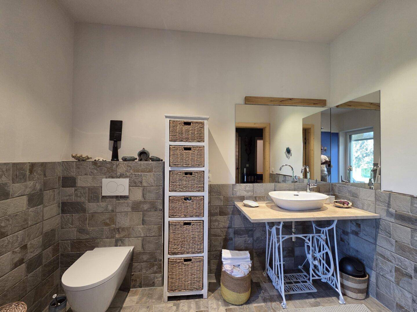 Stilvolles Badezimmer mit Aufsatzwaschbecken, großem Spiegel und gefliesten Wänden.