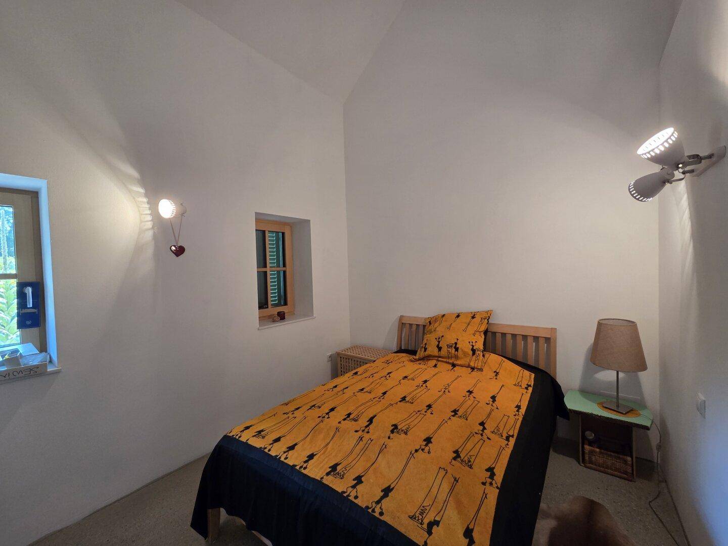 Kleines Schlafzimmer mit Einzelbett, Holzboden und Fenster mit Blick nach draußen.