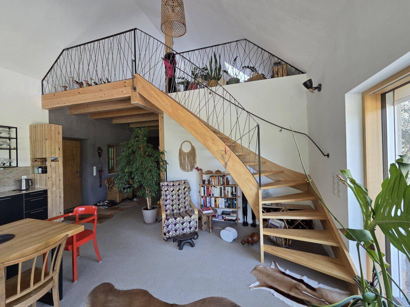 Heller Wohnbereich mit offener Holztreppe zur Galerie und hohen Decken.