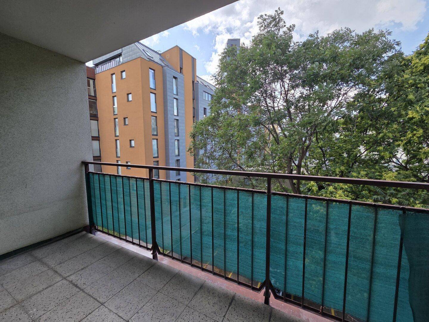 Balkon mit Blick auf umliegende Gebäude und grüne Bäume, ideal zum Entspannen.