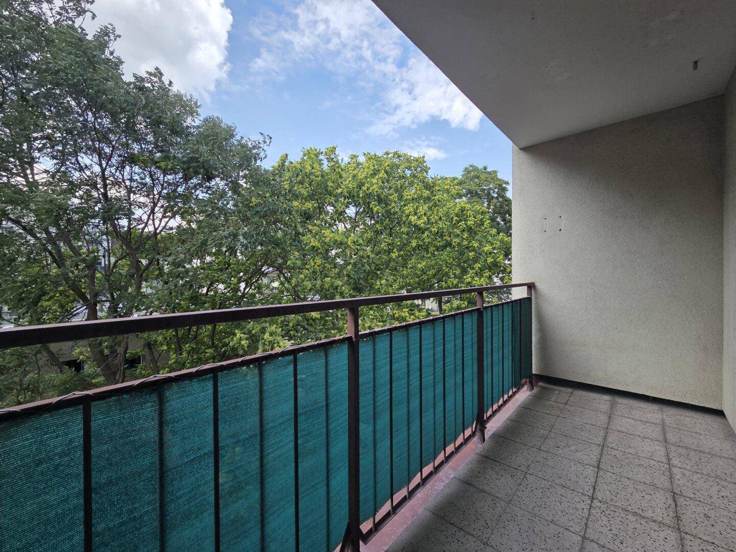 Geräumiger Balkon mit Fliesenboden und weitem Blick ins Grüne und den Himmel.