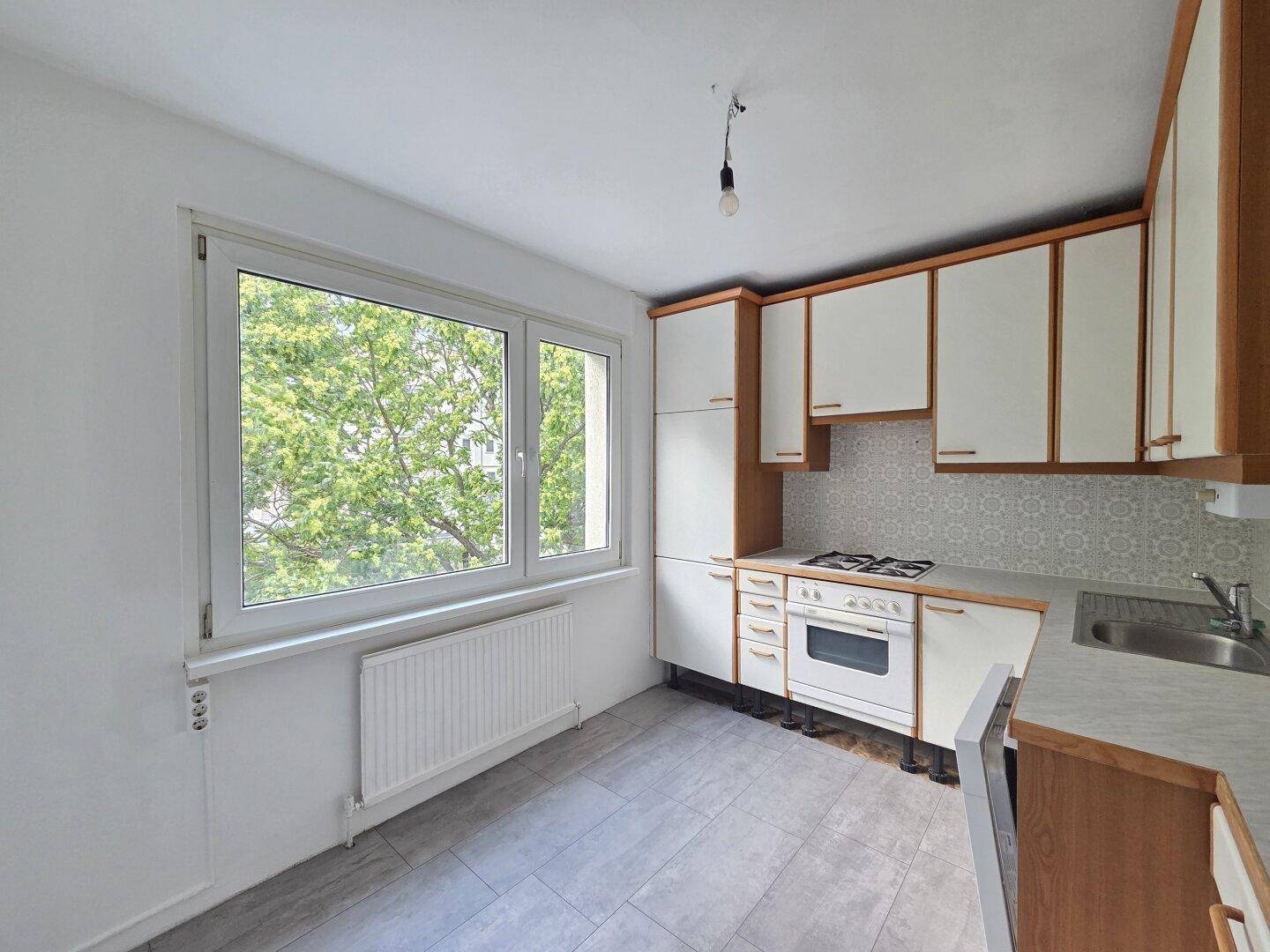 Funktionale Küche mit Gasherd, Fliesenboden und Fenster mit Blick ins Grüne.