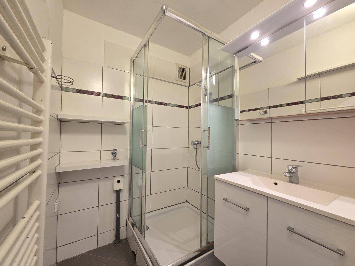 Modernisiertes Badezimmer mit Duschkabine, Waschbecken und beheiztem Handtuchhalter.