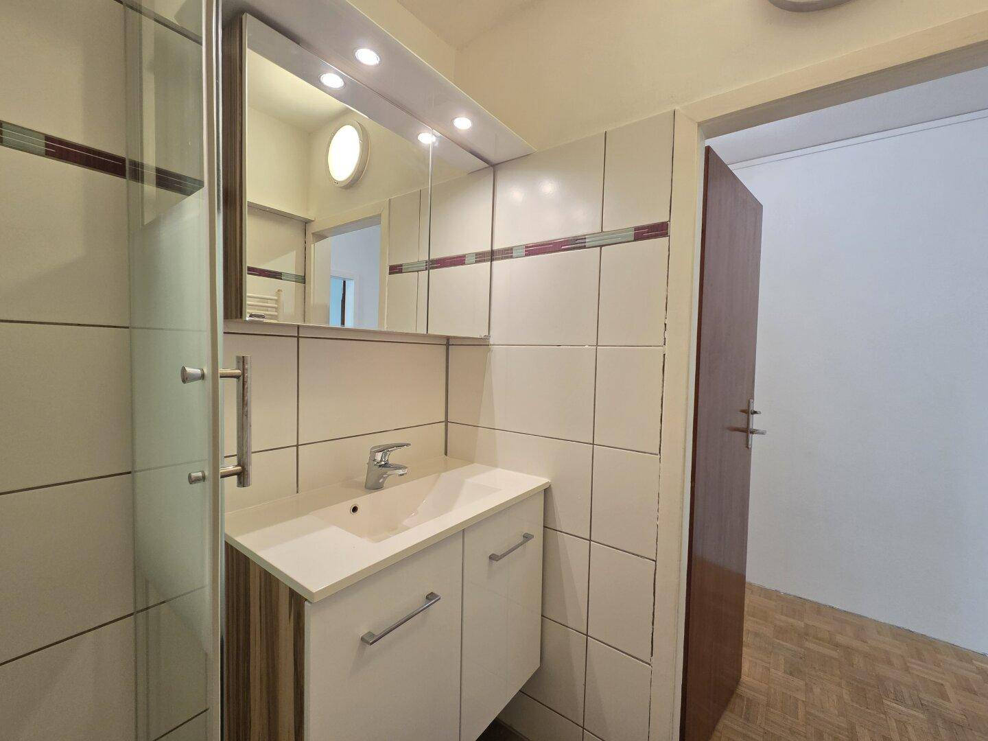 Badezimmer mit Waschbecken, Spiegelschrank und Duschkabine, gut beleuchtet.